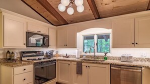 Una cocina con armarios blancos, estufa, microondas y ventana con vista a árboles.