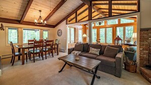 Una sala de estar acogedora con comedor, vigas de madera en el techo, ventanas amplias y una chimenea.