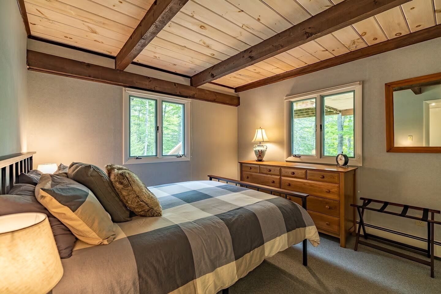 A bedroom with a bed, dresser, and two windows.