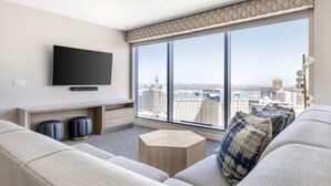 A modern living room with a large window, a flat-screen TV, a sofa, a coffee table, and a desk.