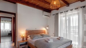 A bedroom with a wooden bed, a bedside lamp, and a view of a room with a window and curtains. - Lithus Retreat with Jacuzzi  & 360° Views (ΧΑΝΙΑ)