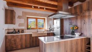 A kitchen with wooden cabinets, a built-in stove, and a window with a mountain view. - Lithus Retreat with Jacuzzi  & 360° Views (ΧΑΝΙΑ)