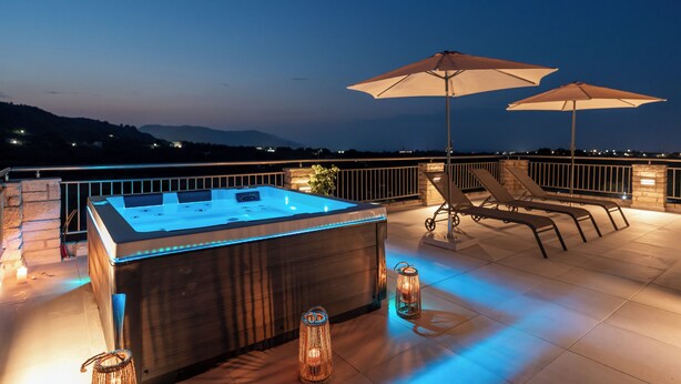 A hot tub with LED lights, two umbrellas, and lounge chairs on a rooftop terrace with a city view at dusk. - Lithus Retreat with Jacuzzi  & 360° Views (ΧΑΝΙΑ)