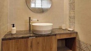 A modern bathroom with a round mirror, wooden vanity, and patterned wall tiles.