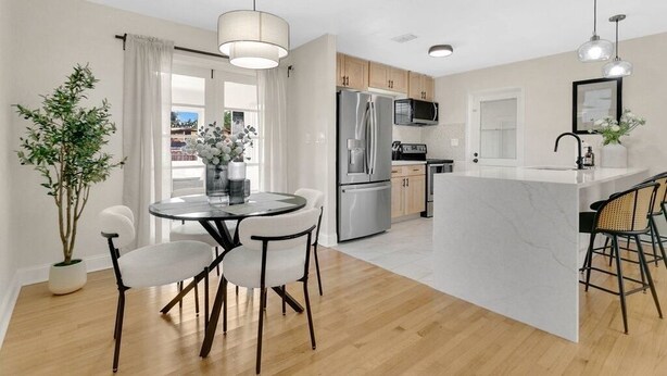 A modern kitchen with a central island, wooden cabinets, stainless steel appliances, and a dining area with a round table and chairs. - Modern Poolside Bungalow in the Heart of Orlando (Orlando)