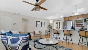 A modern living room with a sofa, coffee table, and chairs. There is a kitchen area with bar stools and a refrigerator. - Modern Poolside Bungalow in the Heart of Orlando (Orlando)
