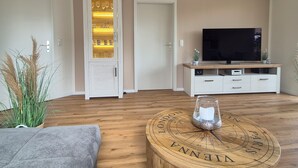Un salon avec un plancher en bois, un téléviseur posé sur un meuble en bois, un buffet blanc et un globe terrestre sur une table ronde en bois.