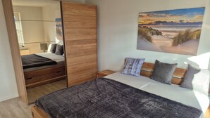 Une chambre à coucher comprenant un lit, une armoire en bois, une table de chevet, une lampe et un tableau représentant une scène de plage.