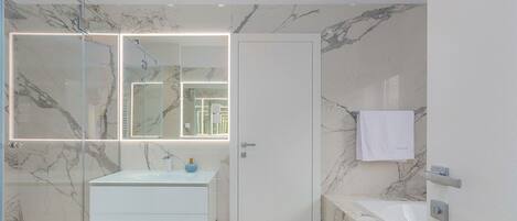 Une salle de bain moderne avec un pare-baignoire en marbre, une douche en verre et un meuble-lavabo blanc agrémenté d’un vase bleu.