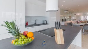A modern kitchen with white cabinets, a black countertop, and a fruit bowl with grapes, oranges, and a pineapple.