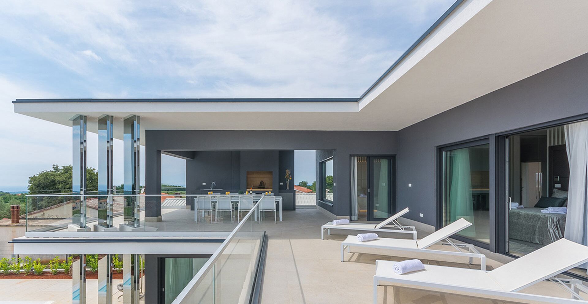 Een moderne buitenruimte met glazen hekwerk, een eethoek en lounge fauteuils.