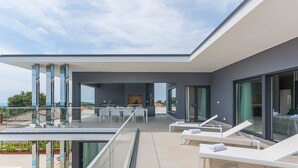 A modern outdoor living area with a glass balustrade, a dining set, and lounge chairs.