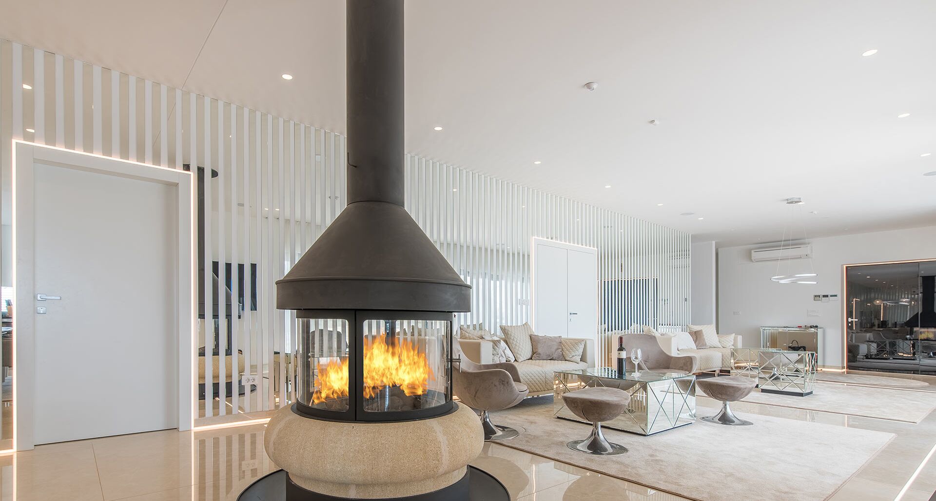 Een moderne woonkamer met een stenen openhaard, witte meubels en een glazen scheidingswand.