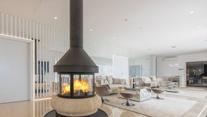 A modern living room with a stone fireplace, white furniture, and a glass partition.