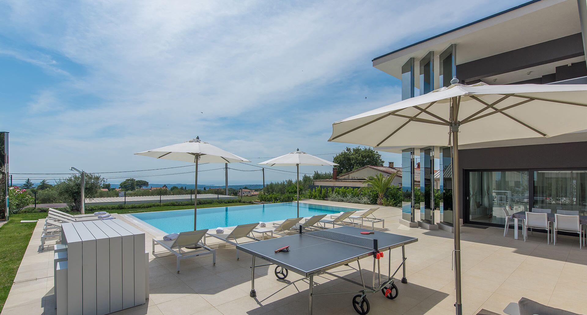 Un área de piscina con sillas de descanso, una mesa de ping pong y sombrillas.