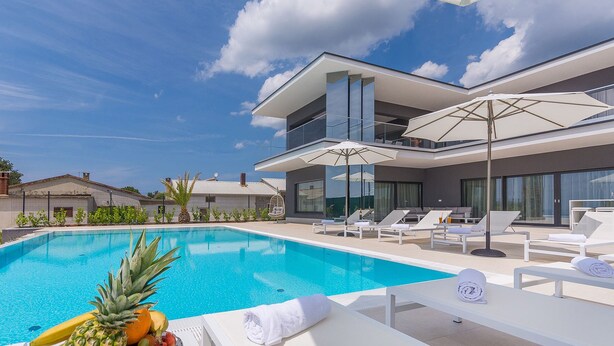 A modern pool area with lounge chairs and umbrellas, surrounded by a two-story building with large windows.