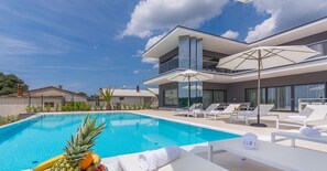 A modern pool area with lounge chairs and umbrellas, surrounded by a two-story building with large windows.