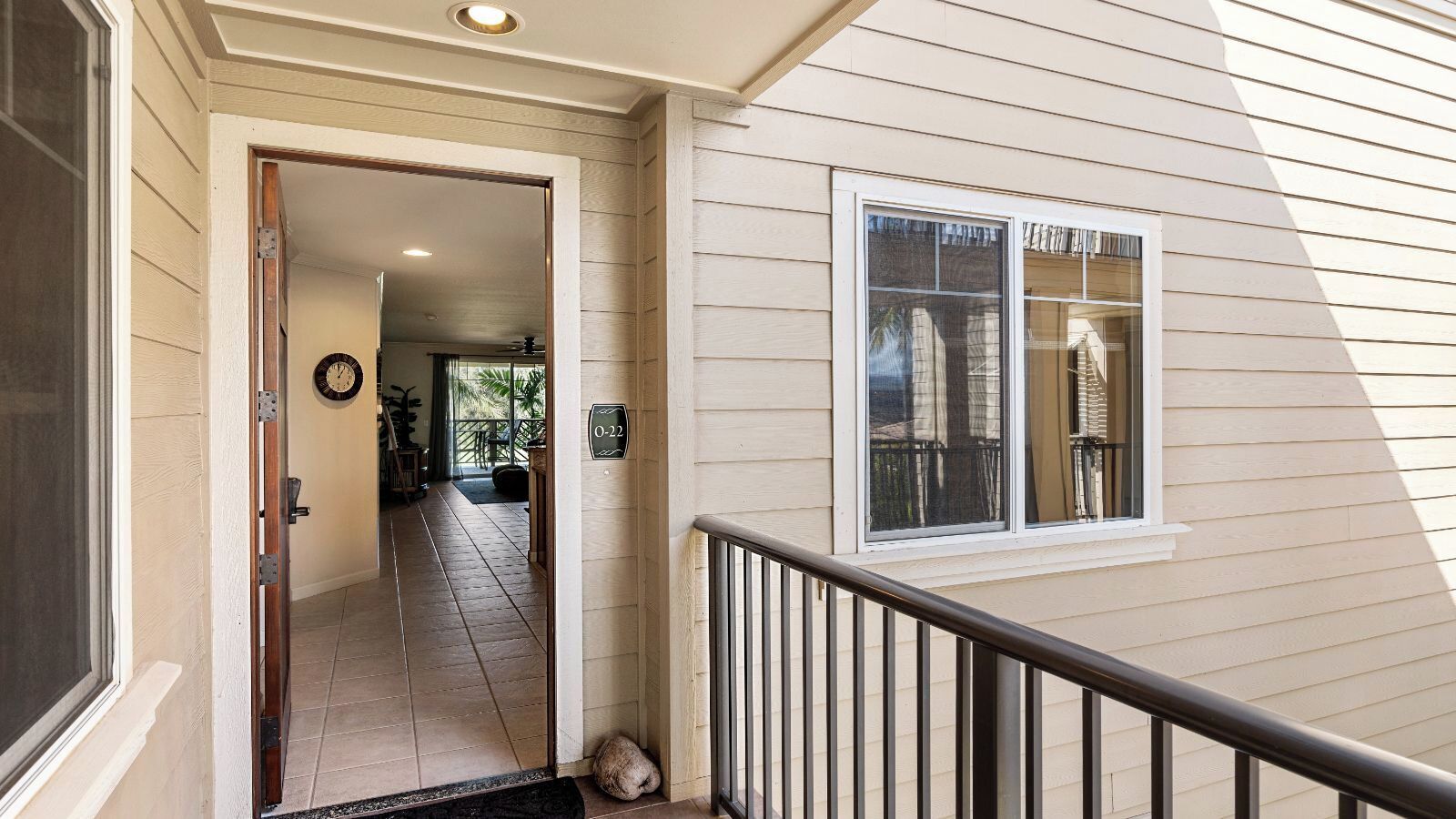 A house entrance with a door leading to a tiled hallway, a window with blinds, and a small porch area.