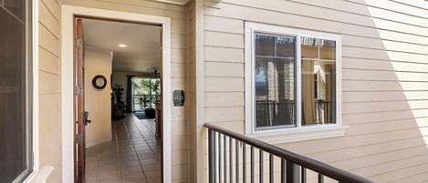 A house entrance with a door leading to a tiled hallway, a window with blinds, and a small porch area.