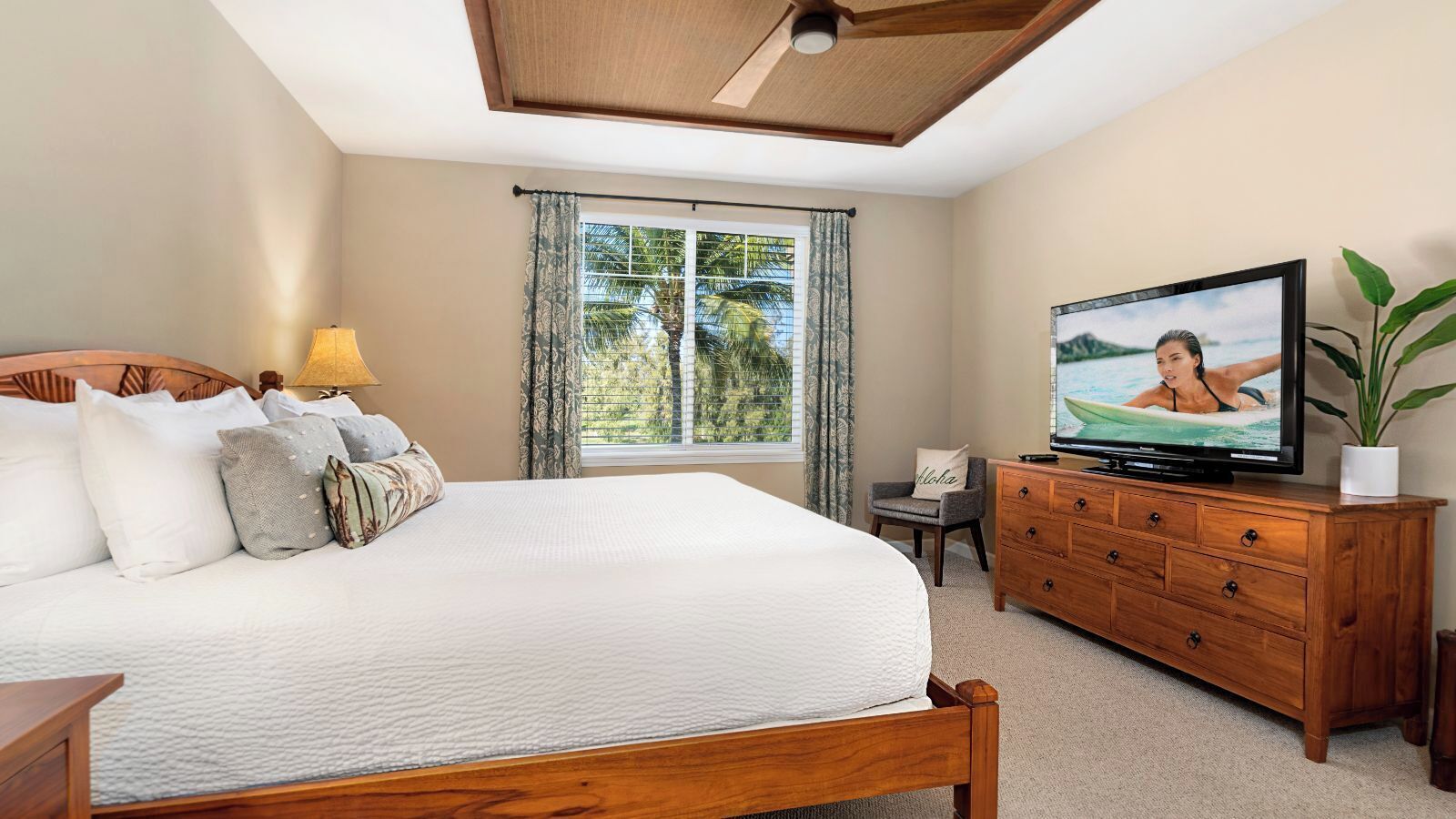 A bedroom with a large bed, a wooden dresser, a television, and a window with curtains.