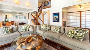 A spacious living area with a sectional sofa, a glass coffee table, and a wooden staircase.
