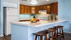 Una cocina con armarios de madera, un refrigerador blanco, una estufa blanca y una isla grande con taburetes.