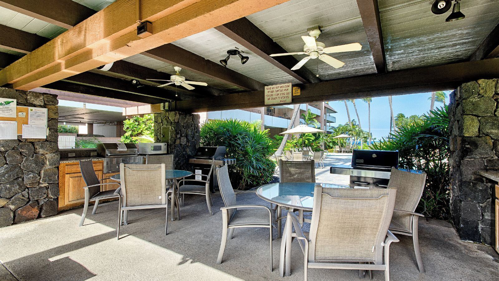 Eine Terrasse im Freien mit einer Steinsäule, einem Grill und einer Sitzecke mit Stühlen und einem Tisch.