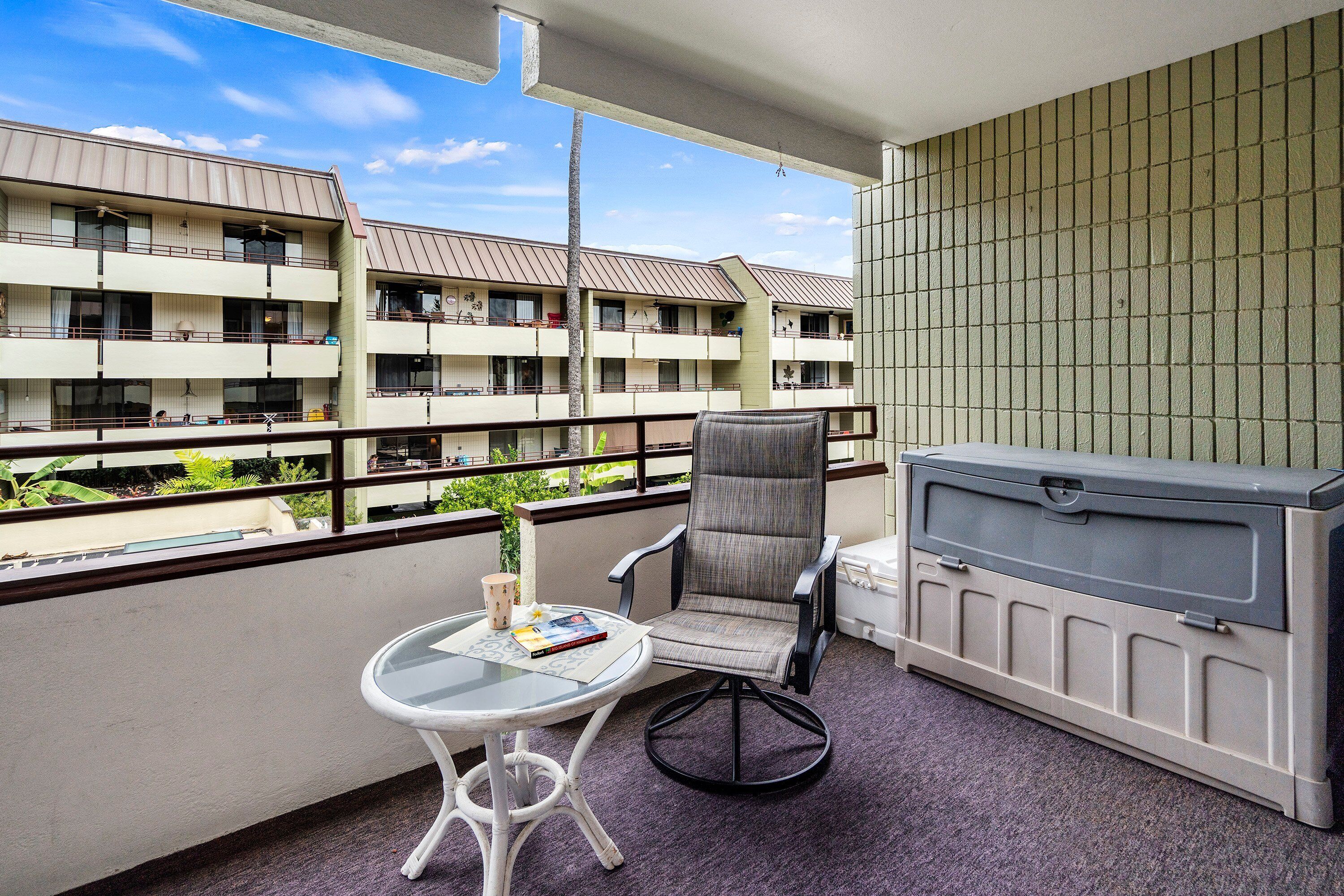 A balcony with a chair, table, and storage unit.