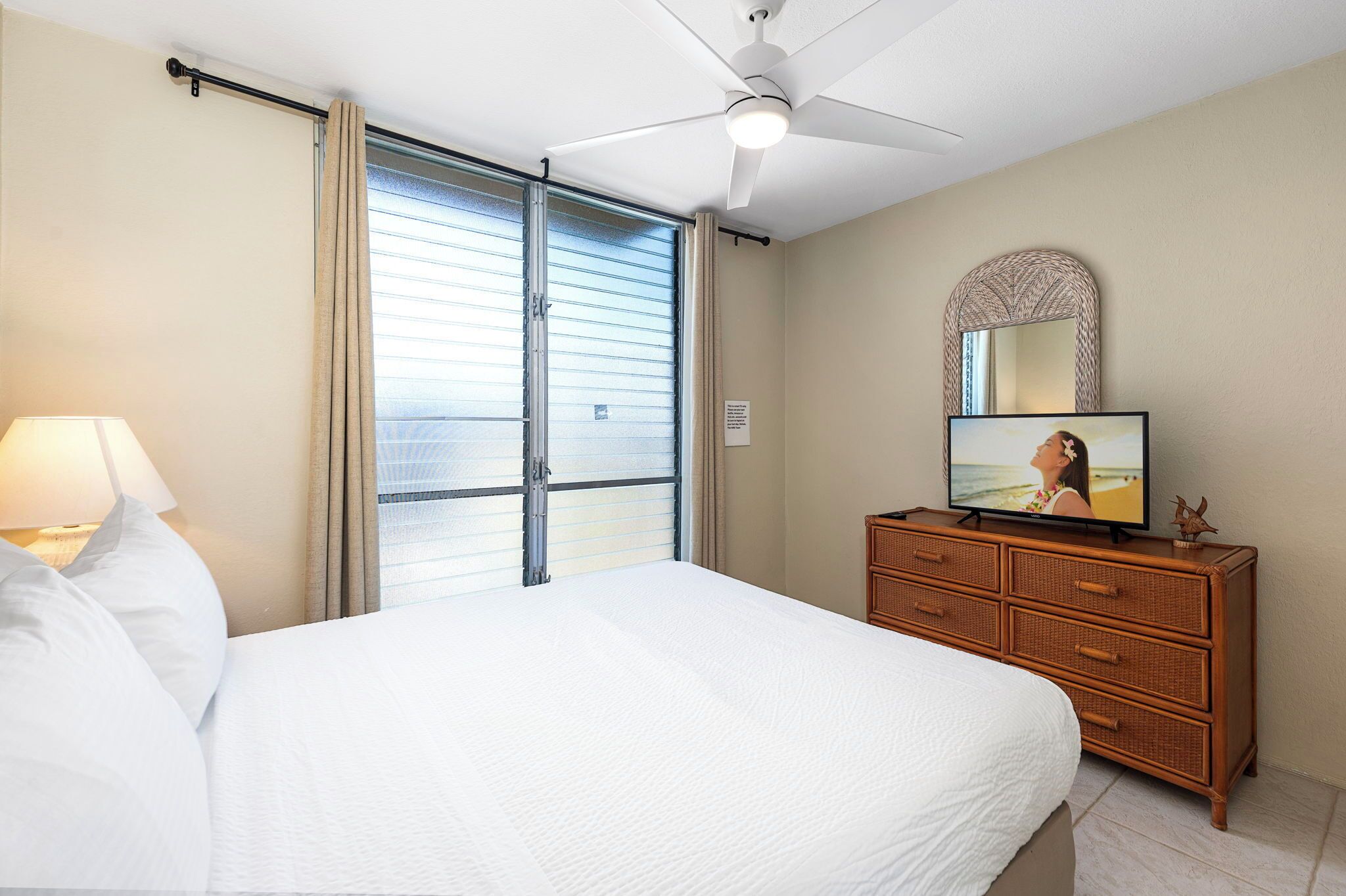 A hotel room with a bed, a dresser, a television, and a ceiling fan.