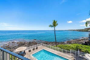 A pool area with a view of the ocean, a palm tree, and a rocky shoreline. - Ocean Front - Direct View of Kailua Bay - Vrkcv (Kailua-Kona)