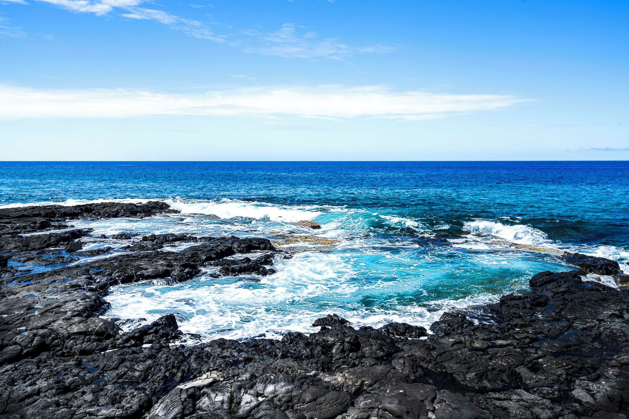 A rocky coastline with waves crashing against the shore under a clear sky.