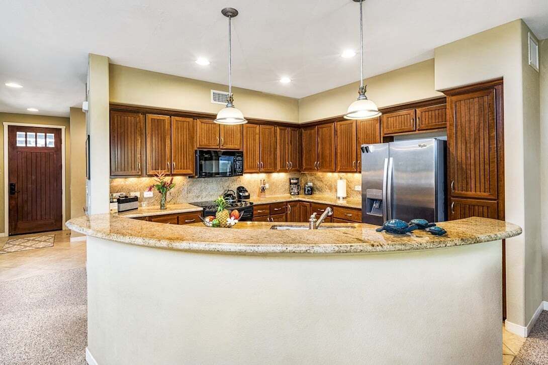 A kitchen with wooden cabinets, a granite countertop, a built-in microwave, a refrigerator, and pendant lighting.