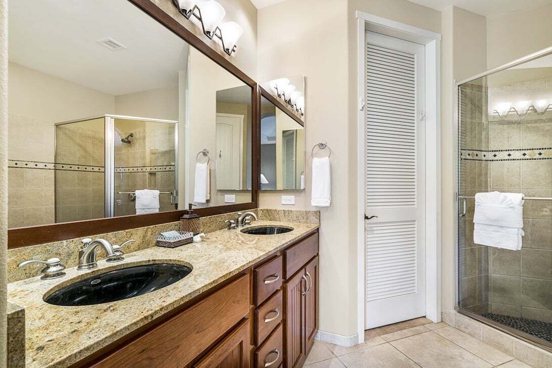 A bathroom with two sinks, a large mirror, and a walk-in shower.