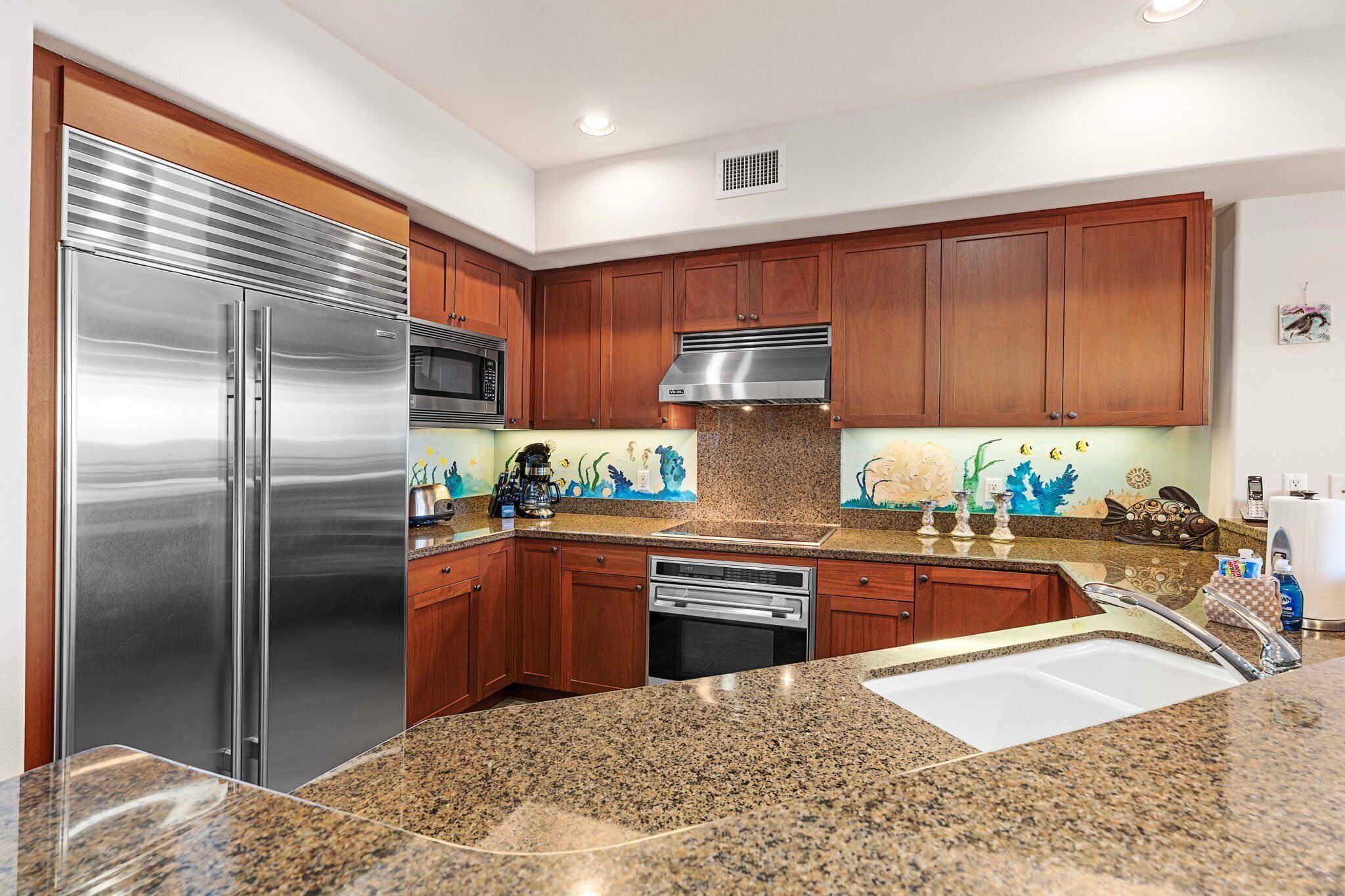 A modern kitchen with stainless steel appliances, granite countertops, wooden cabinets, and decorative backsplash.
