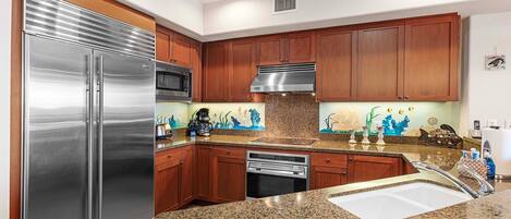 A modern kitchen with stainless steel appliances, granite countertops, wooden cabinets, and decorative backsplash.