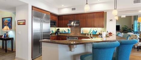 Una cocina moderna con una isla central, electrodomésticos de acero inoxidable, armarios de madera y taburetes de bar azules.