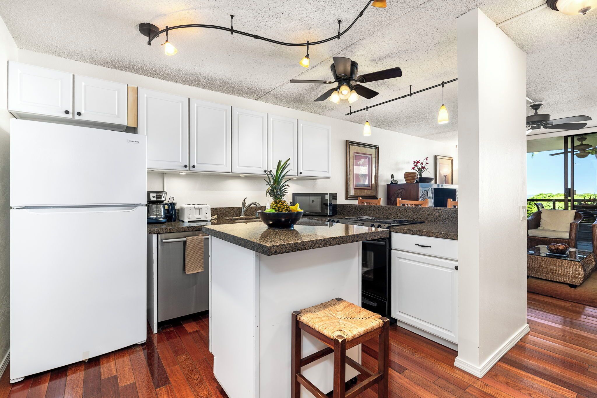 A modern kitchen with white cabinets, a central island, and a ceiling fan.
