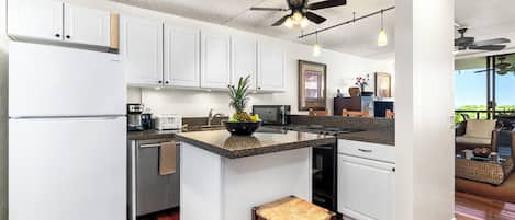A modern kitchen with white cabinets, a central island, and a ceiling fan.