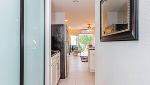 A narrow hallway with a kitchen area featuring a black countertop and white cabinets. - Private Ground Floor Corner Unit - AC & Hawaiian Ocean Views - Vrkcv (Kailua-Kona)