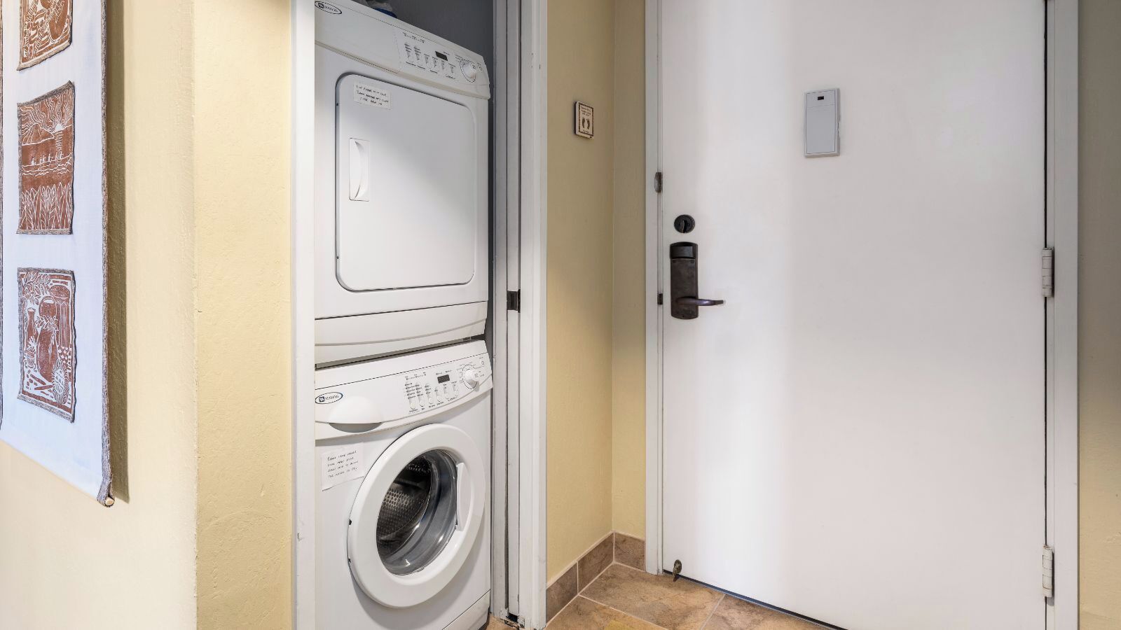 Una lavandería con lavadora y secadora de carga frontal, una puerta con manija y un pequeño cuadro eléctrico en la pared.