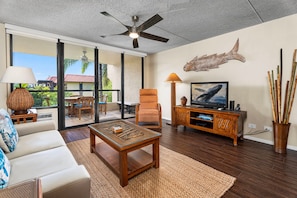 A modern living room with a sofa, coffee table, TV, and a ceiling fan. - AC - Easy Walk to Restaurants Shopping - Concierge Included - Vrkcv (Kailua-Kona)