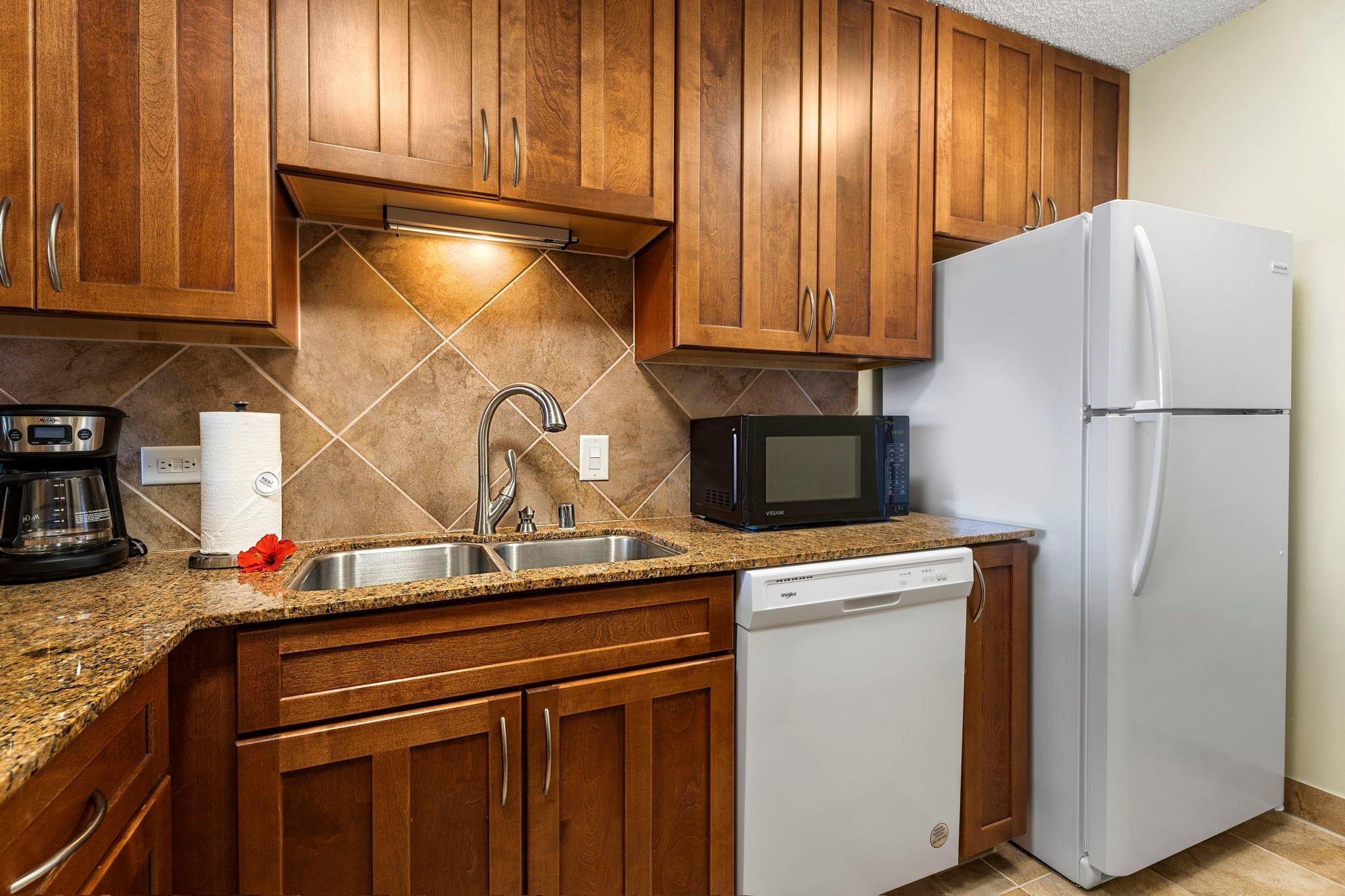 A kitchen with wooden cabinets, a stainless steel sink, a microwave, a refrigerator, and a dishwasher.