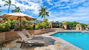 A swimming pool with lounge chairs and a pergola, surrounded by palm trees and potted plants.