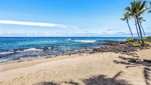 A beach with clear blue water, sandy shore, and palm trees.
