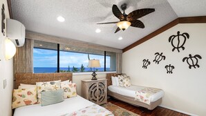 A bedroom with a large bed, a smaller bed, a ceiling fan, a window with a view of the ocean, and decorative wall art. - AC - Beautiful Ocean & Golf Views - 2 Bedrooms w/ Loft - Vrkcv (Kailua-Kona)