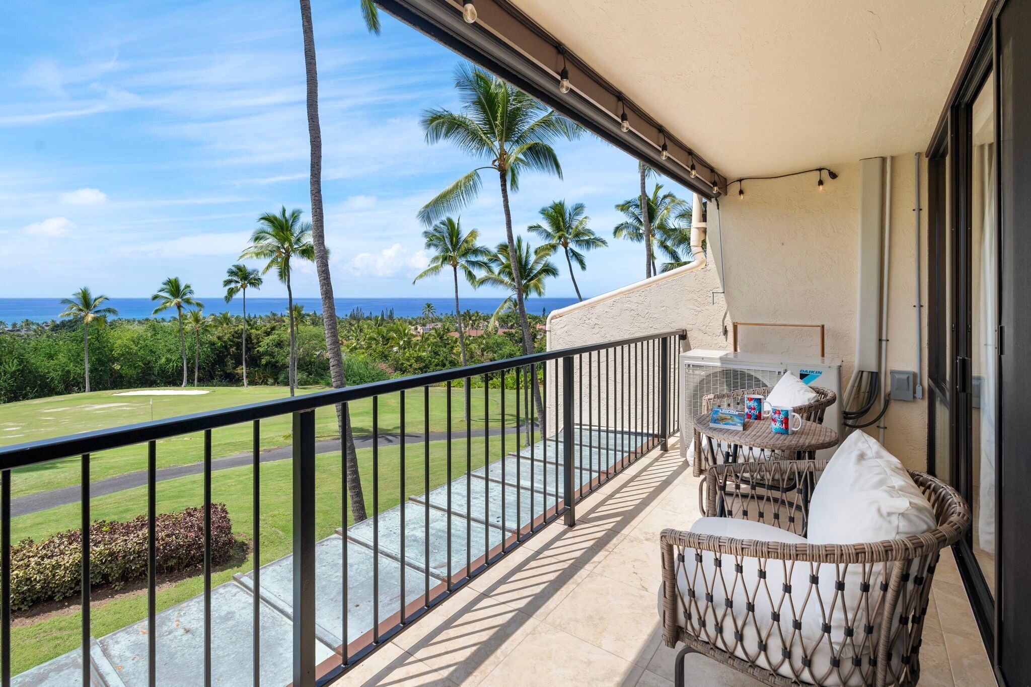 A balcony with a view of the ocean and palm trees, furnished with wicker chairs and a small table.