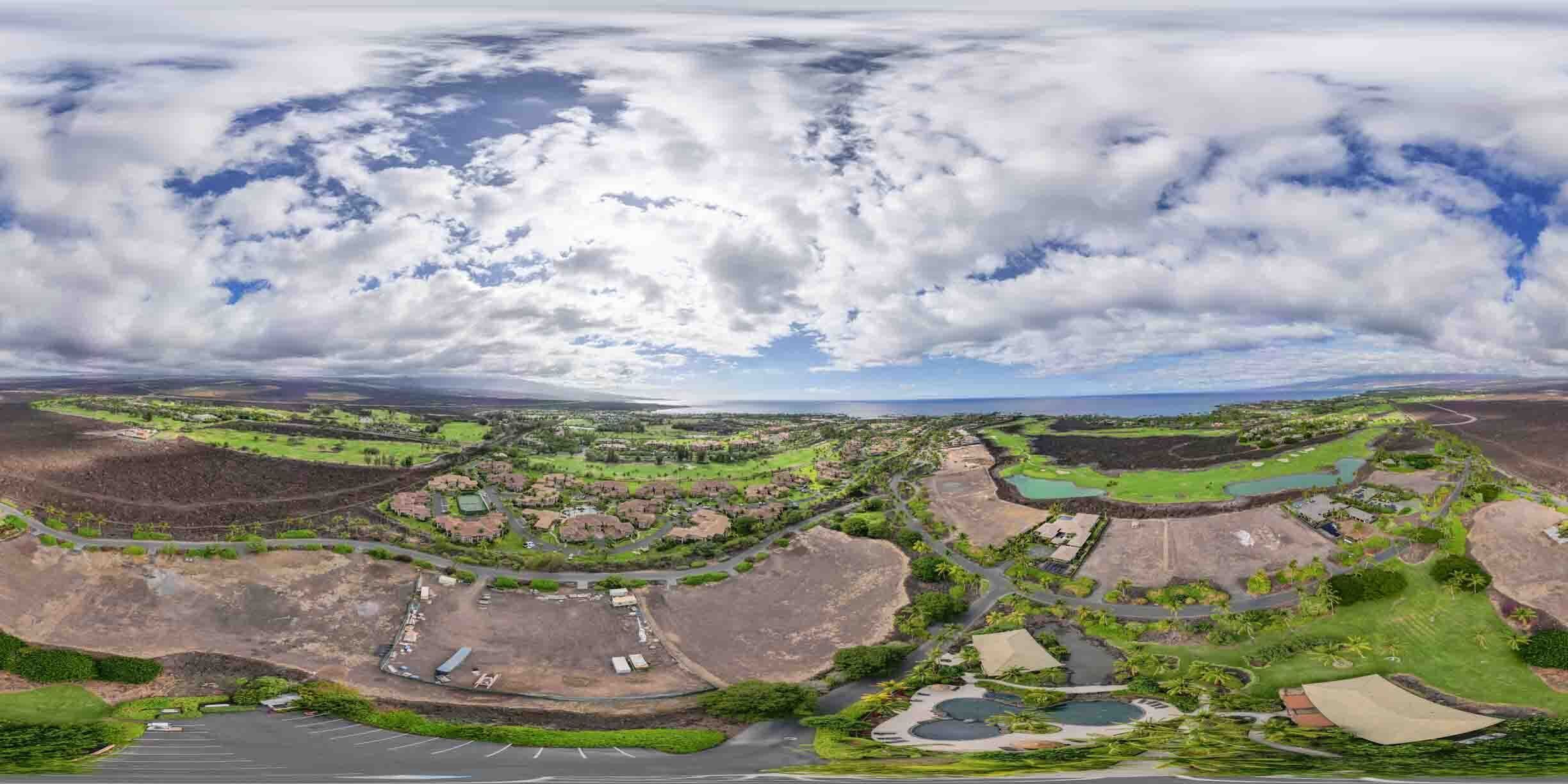 A panoramic view of a coastal area with residential buildings, green spaces, and a parking lot.