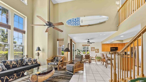 A spacious living area with a high ceiling, a ceiling fan, a surfboard, and a kitchen area with wooden cabinets and a stainless steel refrigerator. - Family-friendly - Pools & Bbqs - Concierge Service - Vrkcv (Waikoloa)