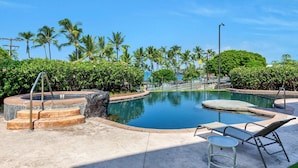 A pool area with a hot tub, lounge chairs, and palm trees.