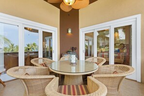 A round glass table surrounded by wicker chairs, with a decorative vase in the center. - Third Floor Penthouse - AC - Excellent Views Ocean - Walk To Beach - Vrkcv (Kailua-Kona)